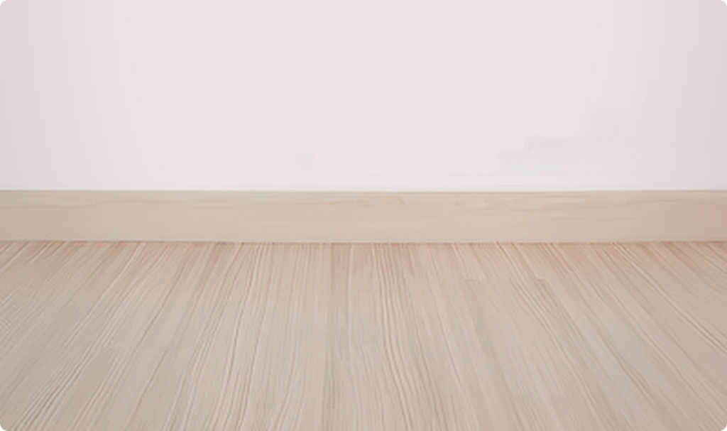 A imagem destaca um piso cerâmico acetinado com textura amadeirada em tons de bege claro. O acabamento é fosco, sem reflexos de luz, transmitindo uma sensação de aconchego e modernidade. O ambiente é complementado por um rodapé de madeira no mesmo tom e uma parede branca lisa ao fundo.